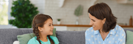 A young girl sitting on a couch next to a practitioner. They smile at each other.