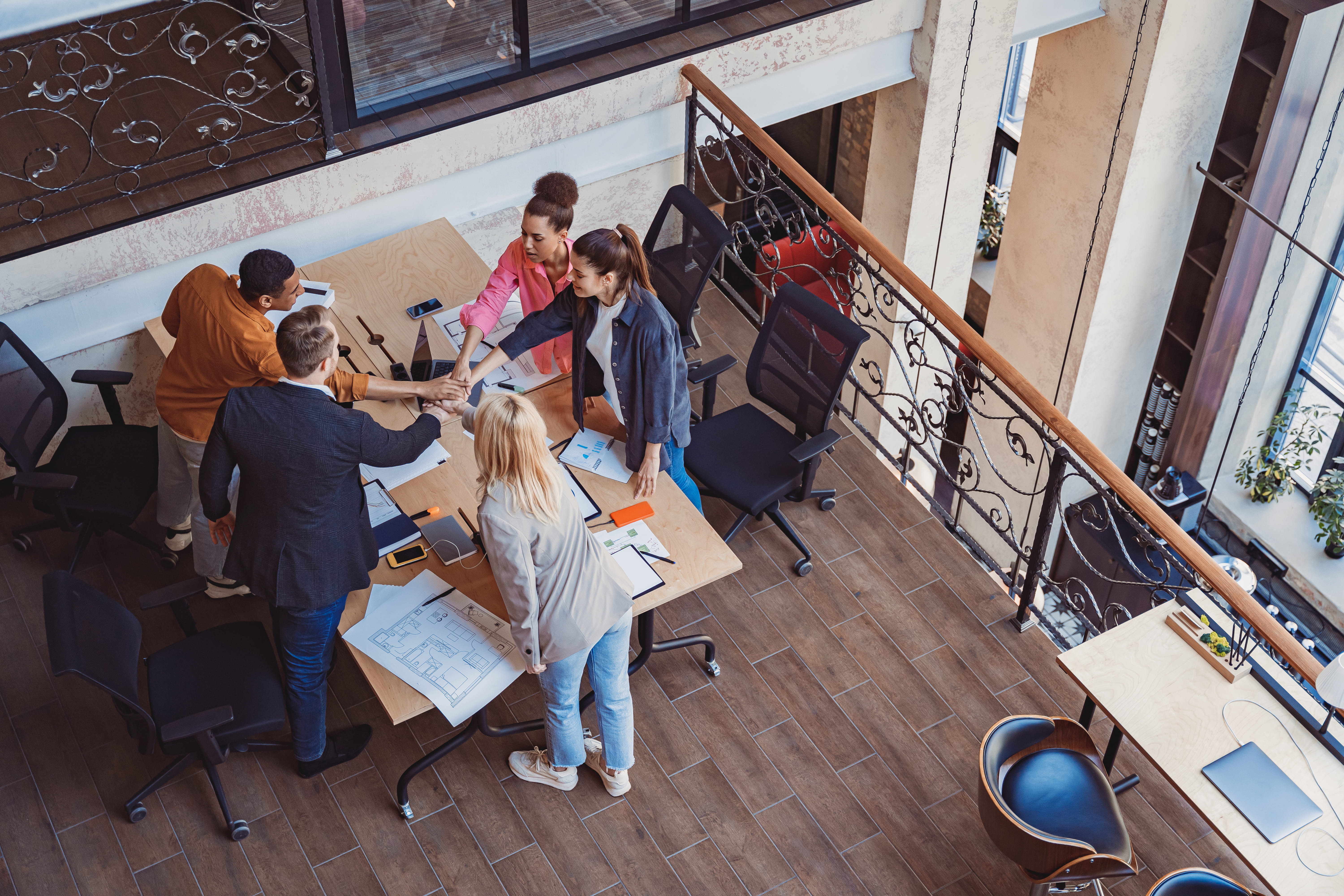 Team members gathered around a table stacking hands in a collaborative office.