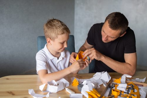 A man helping a young boy use a small tool, sitting together at a table.