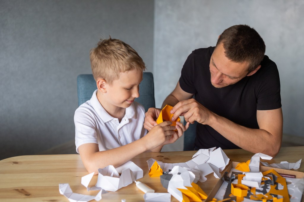 A man helping a young boy use a small tool, sitting together at a table.