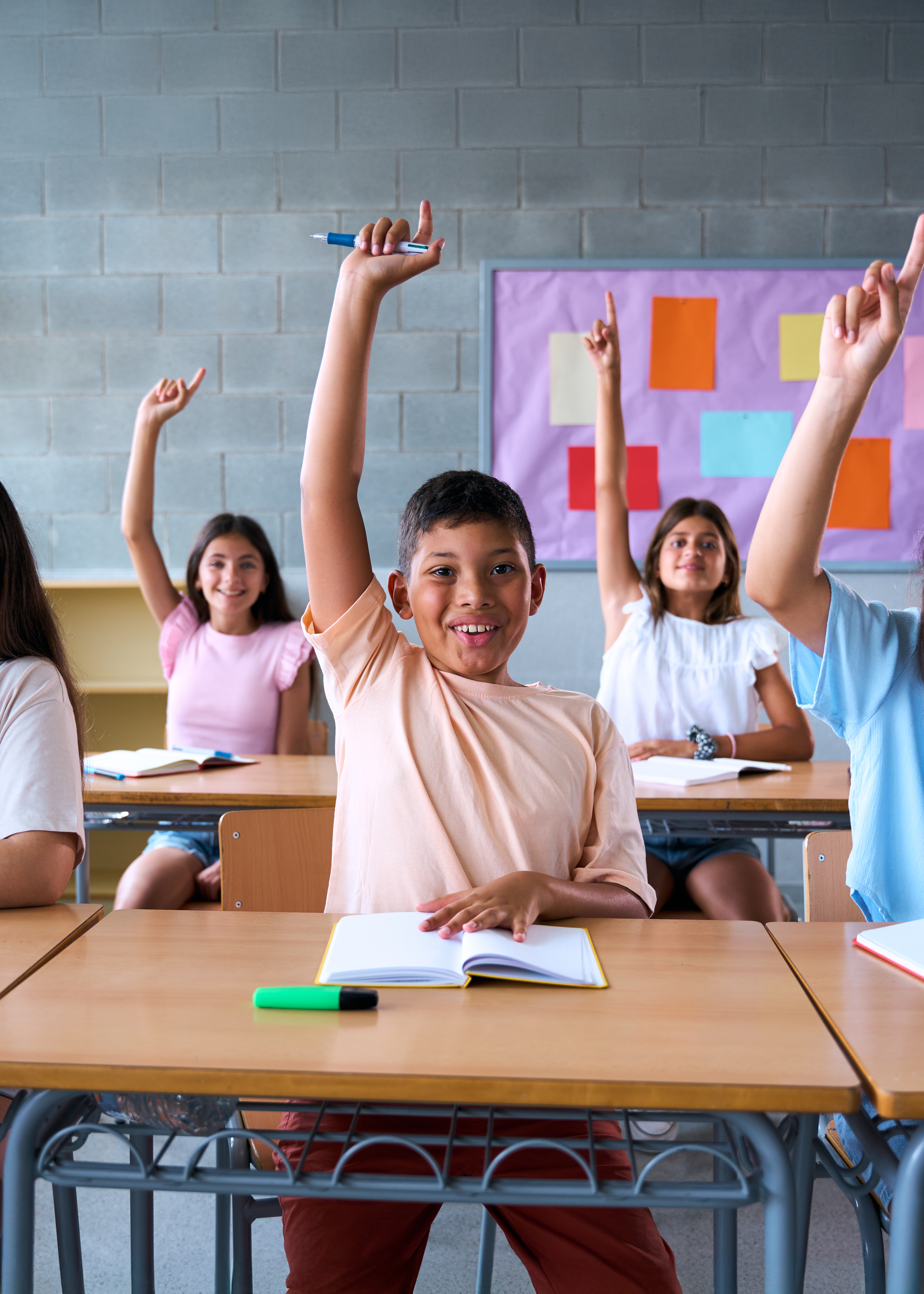 A-group-of-elementary-school-students-sitting-at-desks-in-a-classroom-smiling-and-raising-their-hands-to-answer-a-question