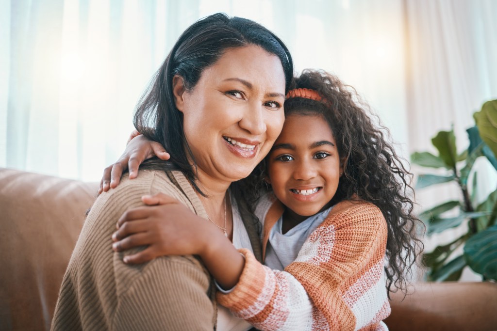 A woman hugging a young girl on a couch, both smiling warmly at the camera.